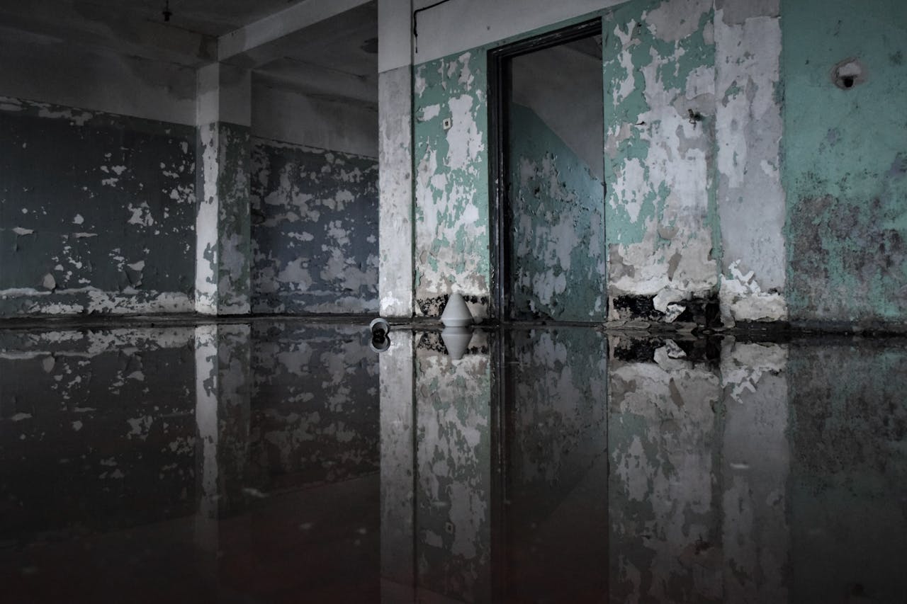 A decaying abandoned room with peeling paint and flooded floor, creating a reflection effect.