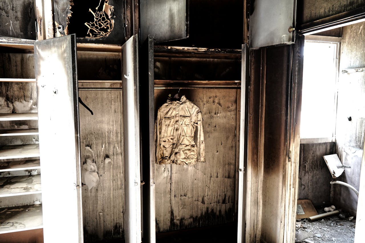 A haunting view of an abandoned, burned-out room with a decaying jacket hanging in a closet.