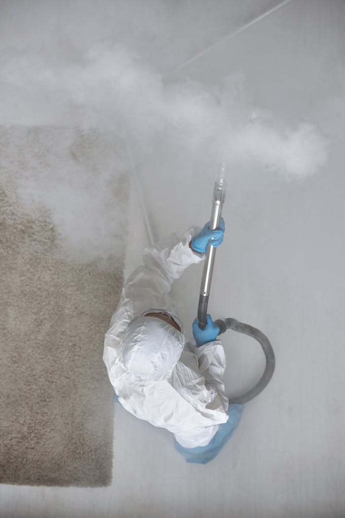 About Person in protective gear fumigating indoors with steam equipment.