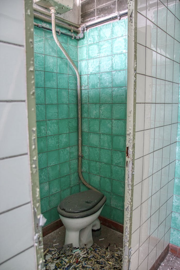 An abandoned restroom with green tiles and broken fixtures, revealing signs of decay.